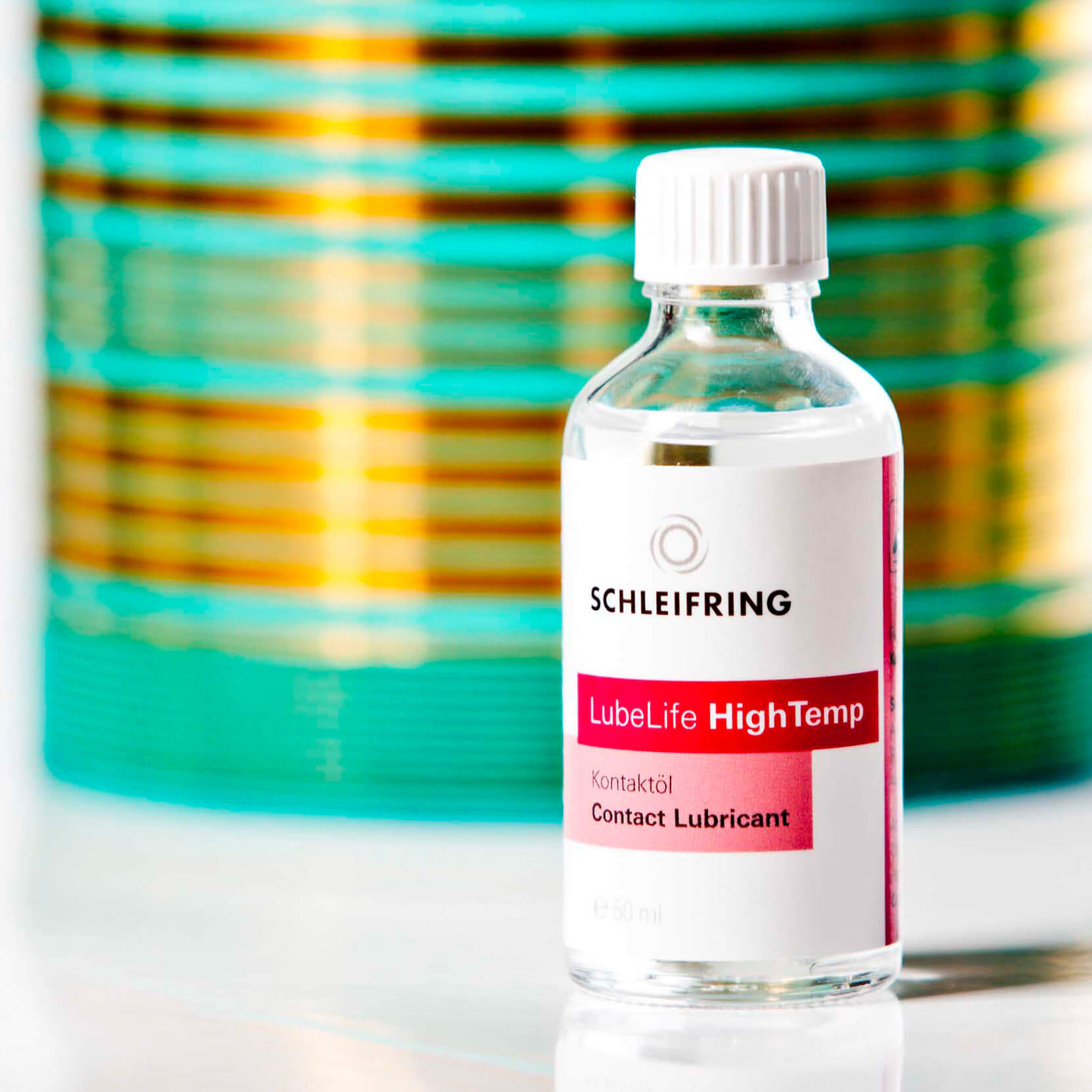 Flasche LubeLife HighTemp Contact Lubricant von SCHLEIFRING vor einem technischen Bauteil.